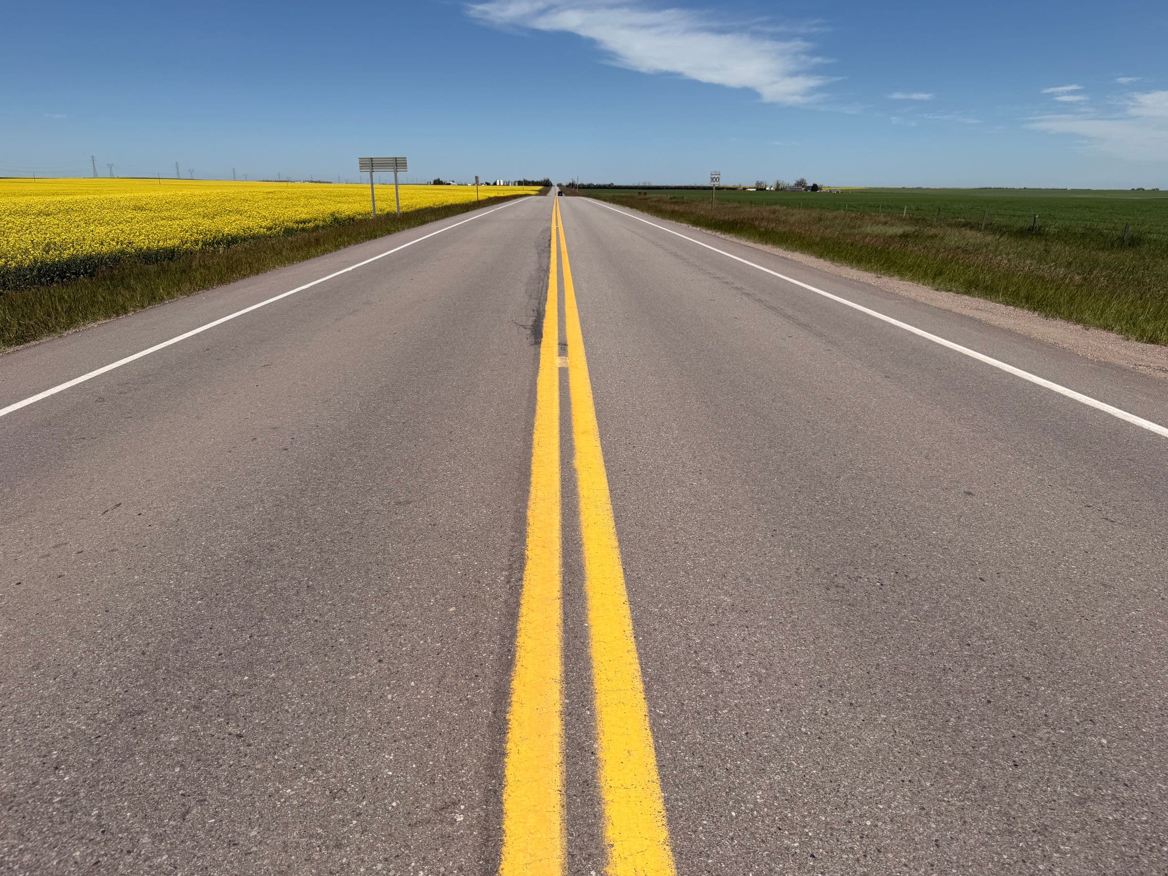 Windshield replacement Clavet area: two-lane highway with a 100 km/h sign between a canola field and green crops