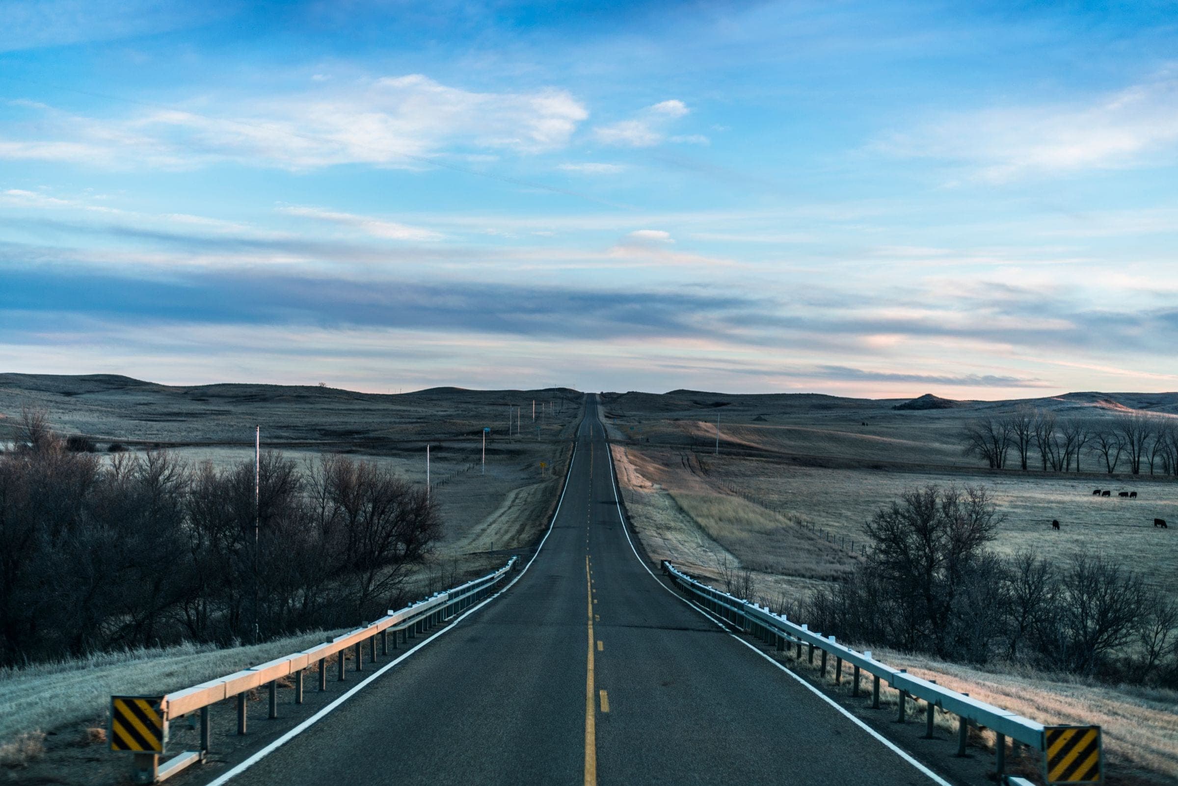 Windshield replacement Langham area: two-lane highway with guardrails crossing a river valley on the prairie at dawn